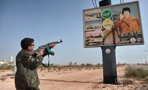 An armed supporter of the Libyan opposition shoots a machine gun at a poster with the image of Muhammar Gaddafi in the captured rebel town of Ras-Lanuf in the east of the country.